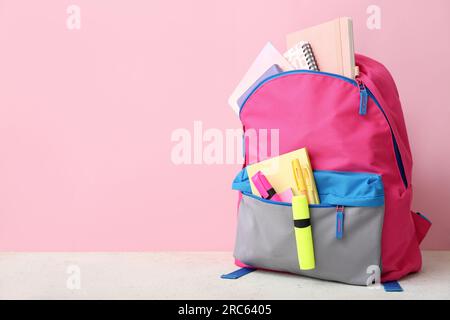 Pink school backpack with notebooks, pens and markers on white table near color wall Stock Photo