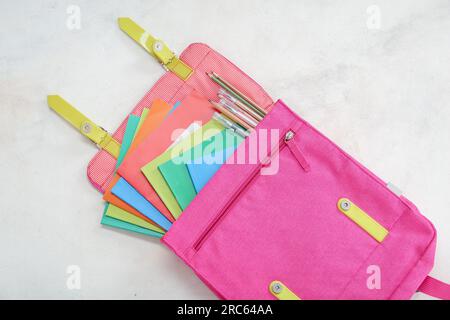 School backpack with different colorful notebooks, pens and pencils on grunge light background Stock Photo