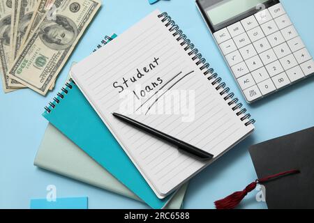 Notebook with text STUDENT LOANS,  calculator, dollar banknotes and graduation cap on blue background Stock Photo