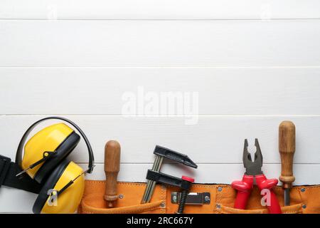 Tool belt with different tools and ear muffs on white wooden background. Labor Day celebration Stock Photo