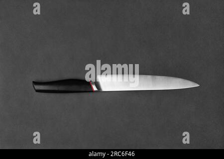 Kitchen knife with a black handle on a black background. Large knife on a dark background. Kitchenware. Knife with a wide blade. Stock Photo