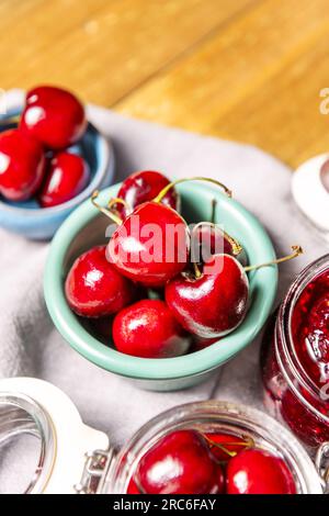 some ripe cherries in glass jars, a green porcelain jar and wooden table Stock Photo