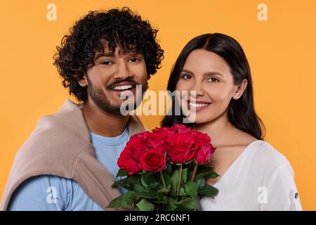International dating. Happy couple with bouquet of roses on yellow background Stock Photo