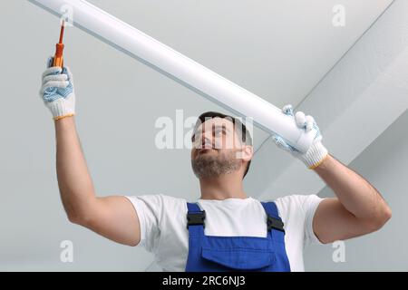 Ceiling light. Electrician installing led linear lamp indoors, low angle view Stock Photo
