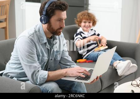 Father working remotely on laptop while his son playing with toys at home Stock Photo