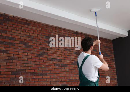 Handyman painting ceiling with roller in room, back view Stock Photo