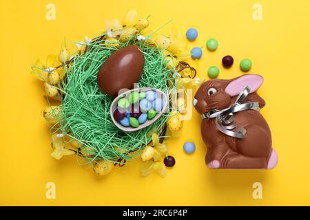 Flat lay composition with chocolate Easter bunny, eggs and candies on yellow background Stock Photo