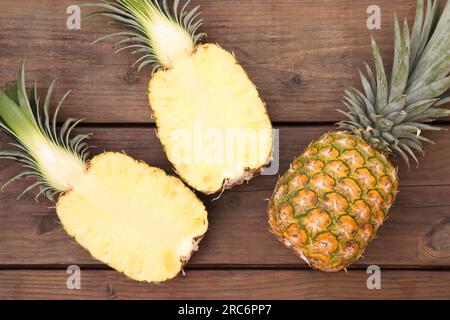 Whole and cut ripe pineapples on wooden table, flat lay Stock Photo