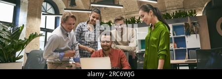 Business professionals at work. Multicultural team, group of young cheerful business people analyzing data, looking at laptop screen while working Stock Photo