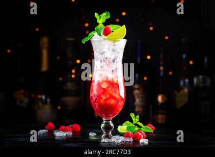 Raspberry lemonade cocktail or mocktail drink with raspberries, syrup, soda, lime, mint and ice, dark bar counter background, copy space Stock Photo