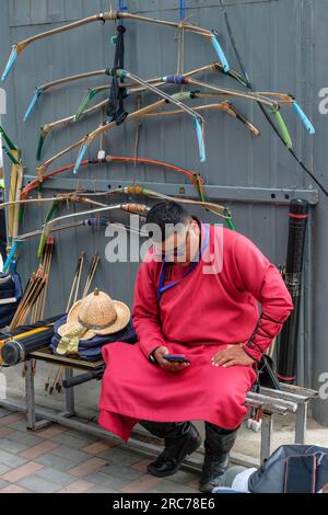 An archer in traditional Mongolian dress shoots an arrow from a bow ...