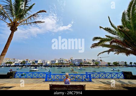 Lanzarote Canary Islands Arrecife centre looking over the Charco  de San Gines water and lone woman on seat with palm trees and   blue sky Stock Photo