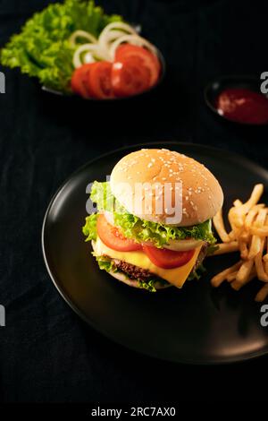 Fresh Tasty burger on cutting board with with french fries, ketchup and cola in glass over black background Stock Photo