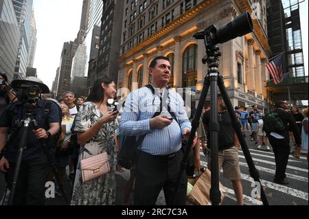 New York, USA. 12th July, 2023. A man holds a remote control for his camera set on a tripod in the middle of 42nd Street and 5th Avenue to capture Manhattanhenge, New York, NY, July 12, 2023. Manhattanhenge is when setting sun (or rising) is aligned with the east-west streets of the main street grid of Manhattan; cloud cover prevented the optimal viewing of the setting sun. (Photo by Anthony Behar/Sipa USA) Credit: Sipa USA/Alamy Live News Stock Photo