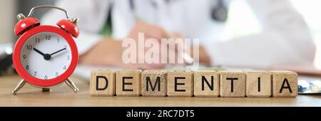 Alarm clock and word dementia on table with blurred doctor in background. Stock Photo