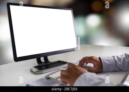 A young businessman is working on the laptop using a desktop computer with a blank screen and an empty copy space display. Stock Photo