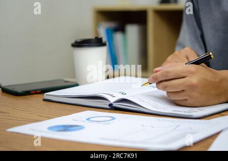 Businessman using pen writing note book planning journal and analysis information statistics document on desk. Stock Photo