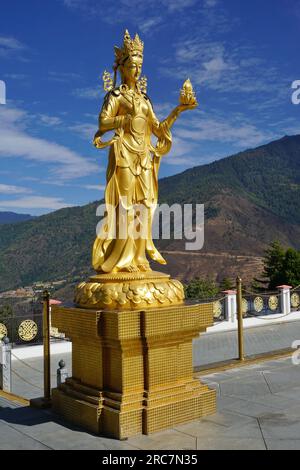 Gilded apsara goddess statue on pedestal in silhouette against blue sky and forested mountains at Buddha Dordenma memorial site near Thimphu, Bhutan Stock Photo