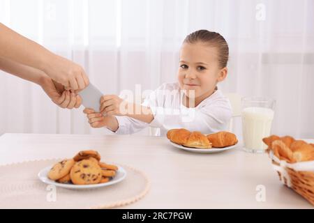 Woman taking away smartphone from her daughter at table indoors, closeup. Internet addiction Stock Photo