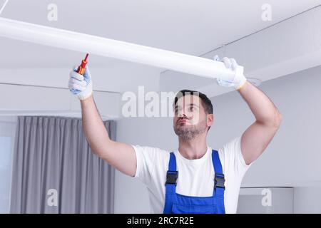Ceiling light. Electrician installing led linear lamp indoors Stock Photo