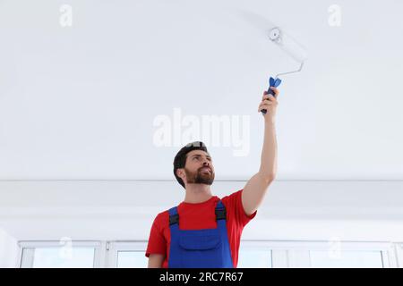 Handyman painting ceiling with roller in room Stock Photo