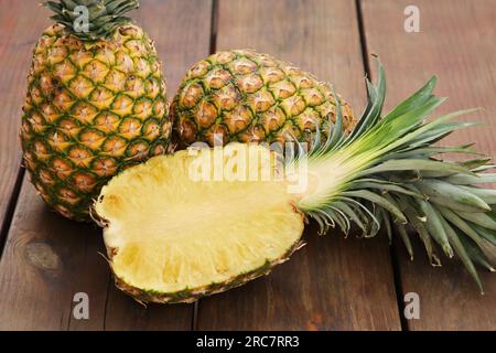 Whole and cut ripe pineapples on wooden table, closeup Stock Photo