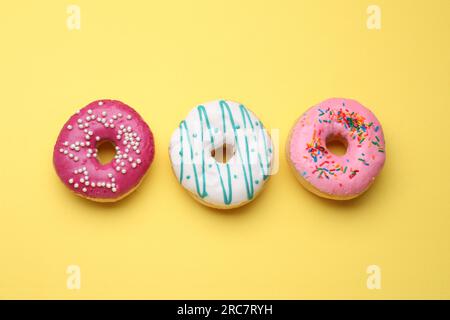 Tasty glazed donuts on yellow background, flat lay Stock Photo