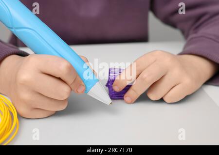 Boy drawing with stylish 3D pen at white table, closeup Stock Photo