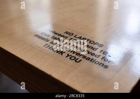 Text on a restuarant table asking you not to use it for your laptop at certain times, but only for what it's intended for, so meals and conversations Stock Photo