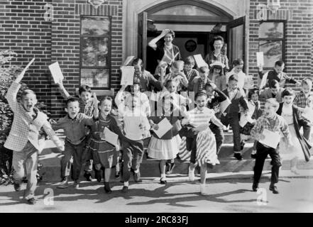 Mt. Carmel, Ohio:   c. 1963 Second graders rush out the door on the last day of school while their teacher bids them goodbye. Stock Photo