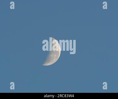 Waning crescent moon on an isolated blue sky background. Stock Photo