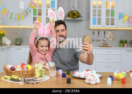 Father with his cute daughter making selfie at table in kitchen. Painting Easter eggs Stock Photo