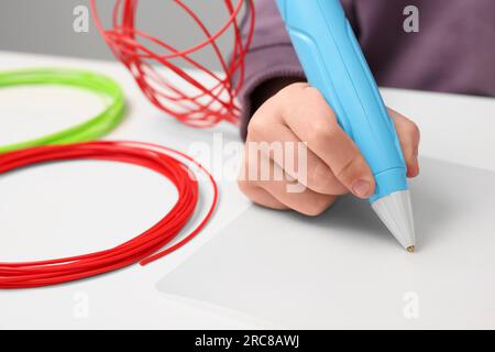 Boy drawing with stylish 3D pen at white table, closeup Stock Photo