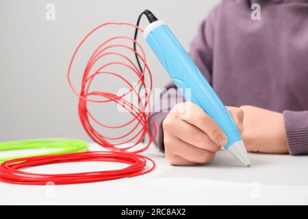 Boy drawing with stylish 3D pen at white table, closeup Stock Photo