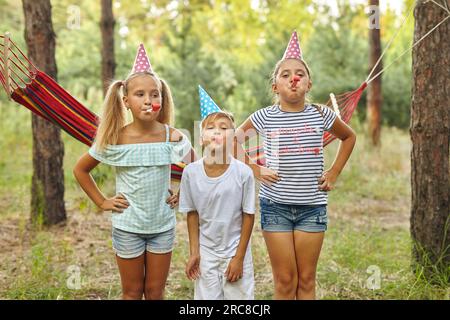 birthday, childhood and celebration concept - happy kids blowing party horns and having fun in summer outdoors Stock Photo