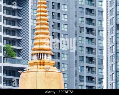 Traditional golden pagoda at a Buddhist temple in Thailand in front of a high rise, modern condominium located in Bang Na on the outskirts of Bangkok. Stock Photo