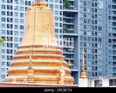 Traditional golden pagoda at a Buddhist temple in Thailand in front of a high rise, modern condominium located in Bang Na on the outskirts of Bangkok. Stock Photo