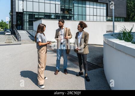 Group of business people walk outside in front of office buildings. Businessman and two businesswomen sharing experience ideas and tactic for successf Stock Photo