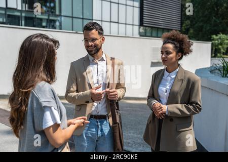 Group of business people walk outside in front of office buildings. Businessman and two businesswomen sharing experience ideas and tactic for successf Stock Photo