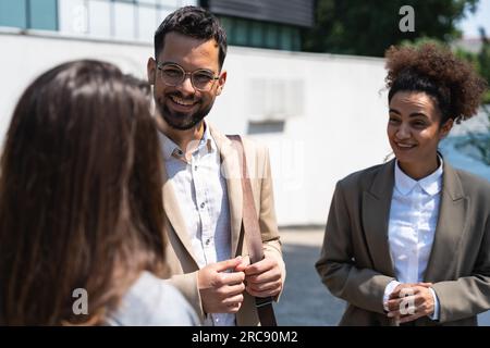 Group of business people walk outside in front of office buildings. Businessman and two businesswomen sharing experience ideas and tactic for successf Stock Photo