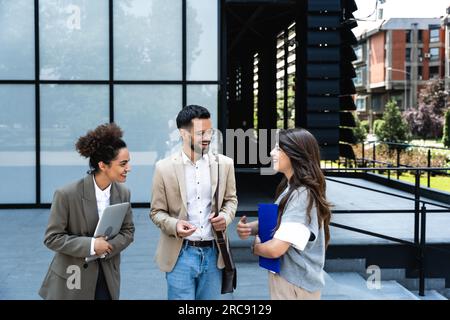 Group of business people walk outside in front of office buildings. Businessman and two businesswomen sharing experience ideas and tactic for successf Stock Photo