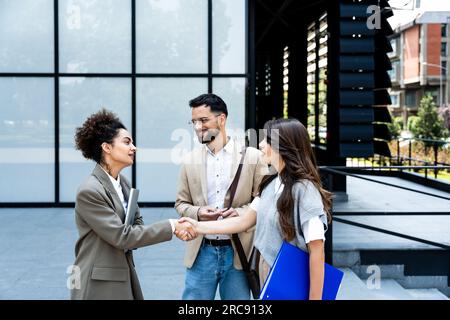 Group of business people walk outside in front of office buildings. Businessman and two businesswomen sharing experience ideas and tactic for successf Stock Photo