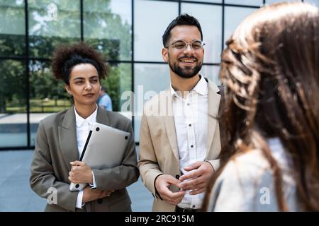 Group of business people walk outside in front of office buildings. Businessman and two businesswomen sharing experience ideas and tactic for successf Stock Photo