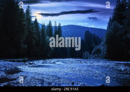 nature scenery with mountain river at night. green environment background with stones on the shore and forested hills in full moon light Stock Photo