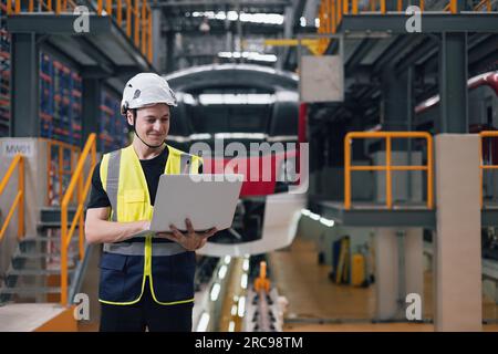 Technician Engineer maintenance service electric train with laptop computer in train repair depot. Train designer in factory. Stock Photo