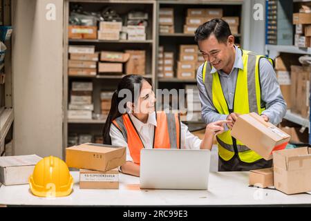 senior engineer manager supervisor working with young woman engineer staff worker in factory hardware parts store inventory room Stock Photo