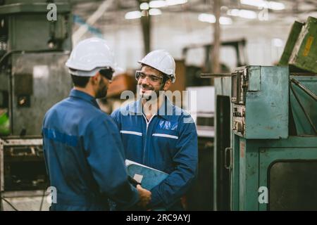engineer worker male hispanic indian male teamwork happy working together in heavy metal industry steel lathe CNC factory Stock Photo