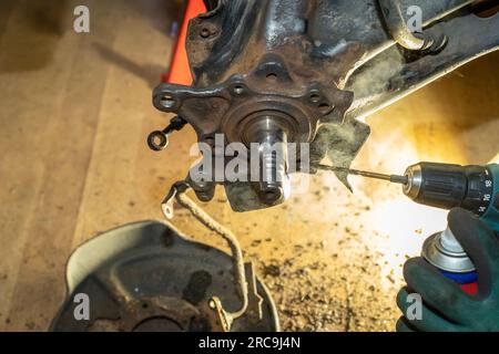 The car mechanic drills a thread on the rear wheel hub bearing and sprays the process with oil to cool it. Auto service. Repairing. Workshop. Stock Photo