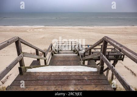 Blick von der Strandtreppe auf den darunter liegenden, menschenleeren Weststrand von List/Sylt. Der graue Himmel hängt voller Feuchtigkeit Stock Photo