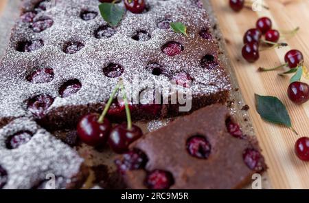 Chocolate cake or brownies with cherries and powdered sugar on a wooden table Stock Photo